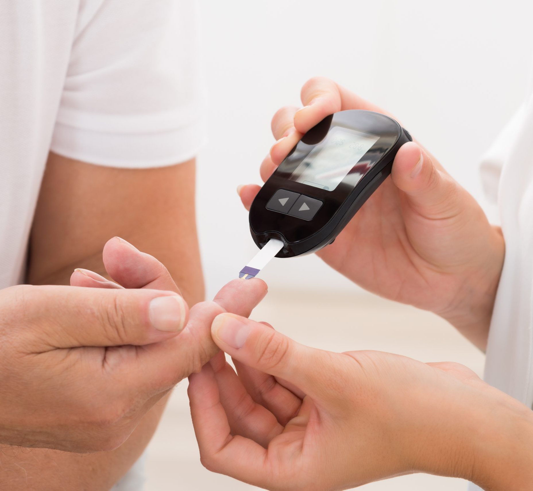 Close-up Of Doctor's Hand Using Glucometer On Patient's Finger