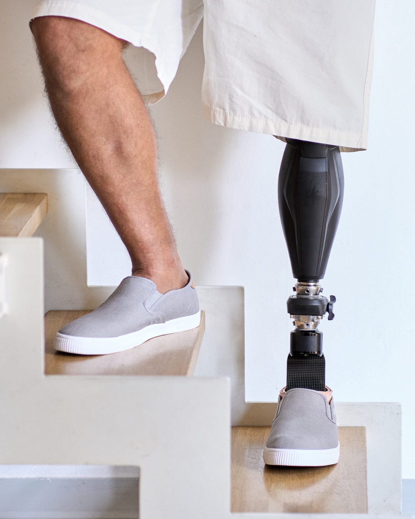 Man amputee with prosthetic leg disability on above knee transfemoral leg prosthesis artificial device stands on feet on stairs, close up. People with amputation disabilities everyday life.